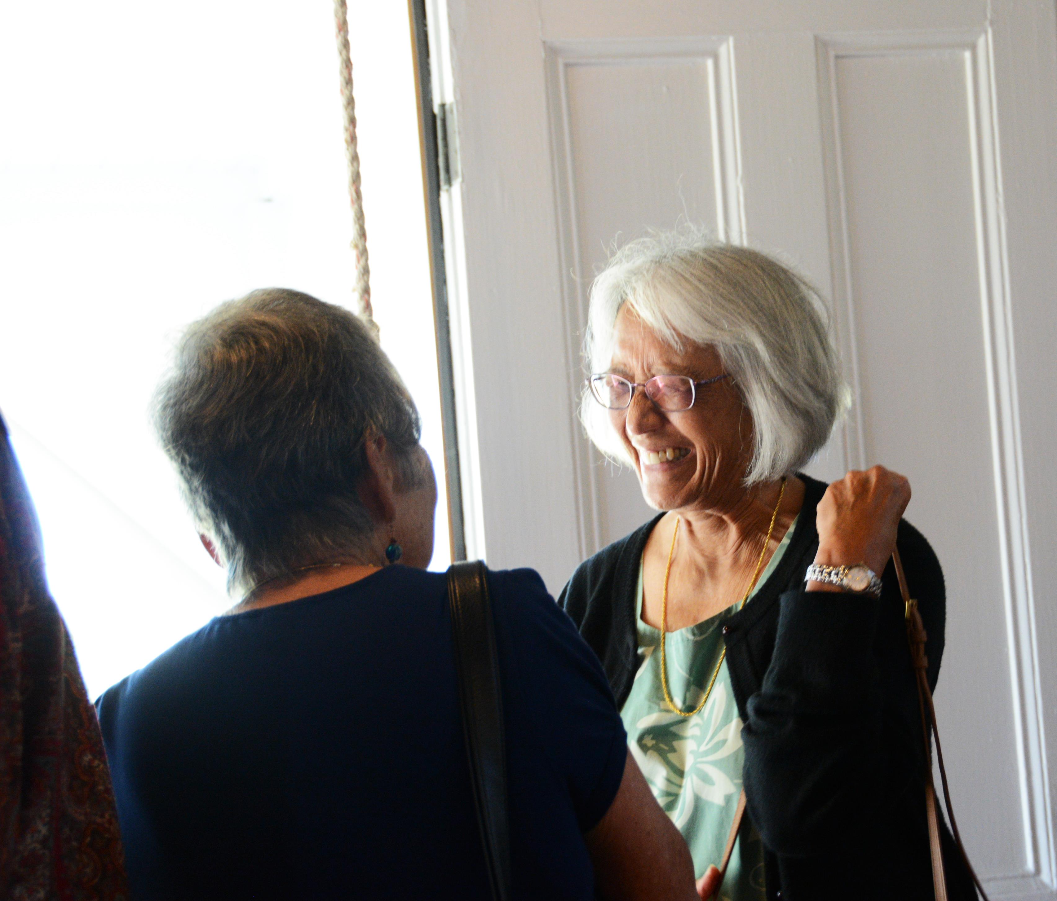 Two seniors share a joyful conversation inside a bright room filled with sunlight.