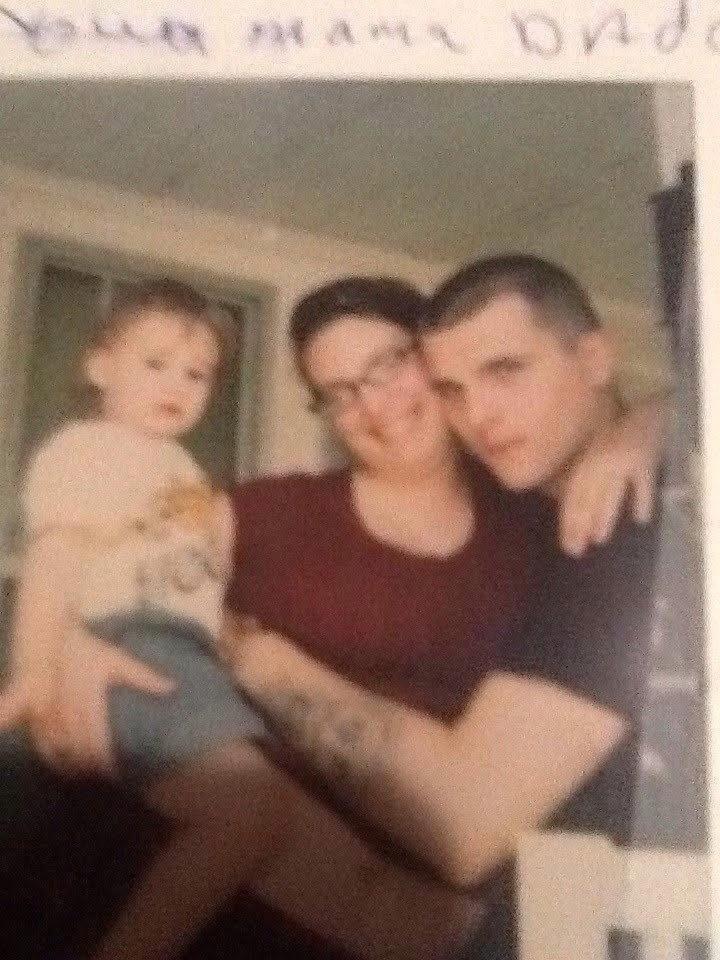 A couple lovingly hold their toddler in a warm domestic environment, smiling warmly.