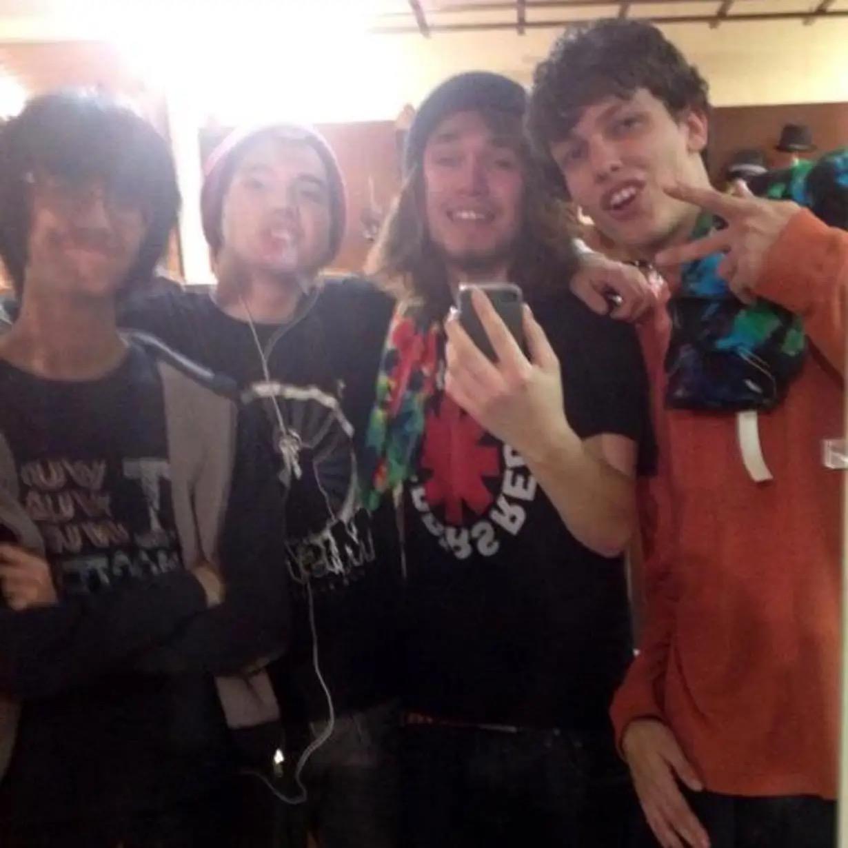 Four young men smile and pose together in a casual indoor gathering, enjoying their time.