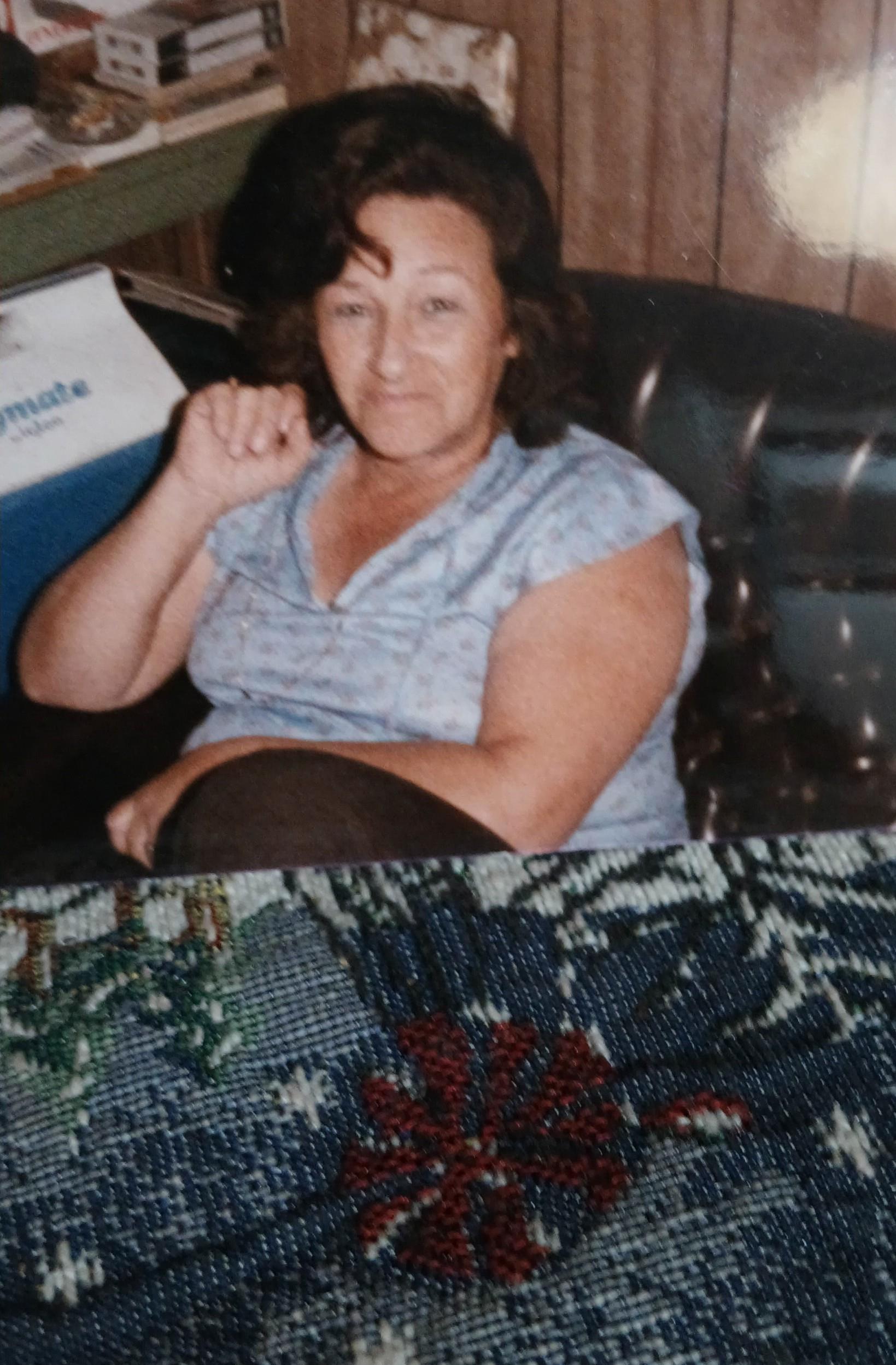 A woman smiles and raises her hand while sitting comfortably in a casual indoor environment.