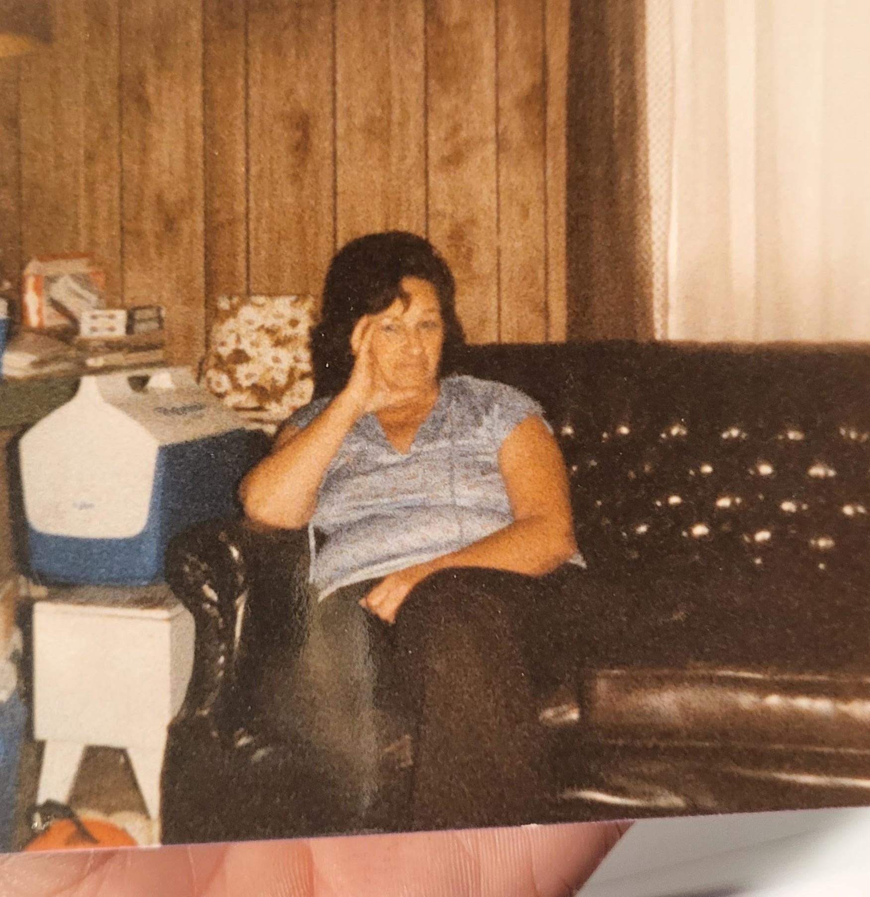 A woman sits on a black couch, seemingly lost in thought, surrounded by a warm, homey environment.