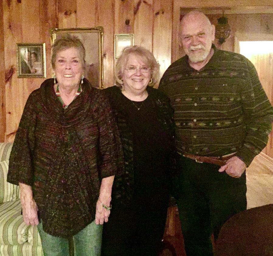 Three friends pose together in a warm, inviting cabin living room, sharing smiles.
