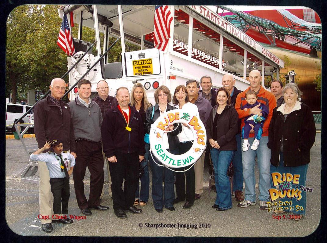A cheerful, diverse group celebrates by a boat, waving flags and sharing smiles.