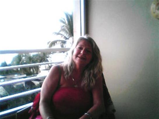 A woman sits on a balcony, smiling while enjoying the warm ocean breeze and scenic views.