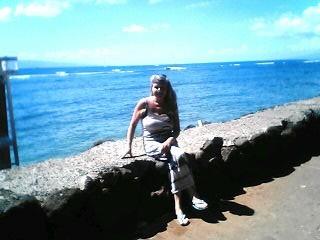 A woman relaxes on a rocky edge near the ocean, basking in the sun on a clear day.