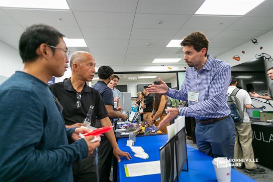 Two attendees discuss technology developments with a presenter at a bustling expo event.