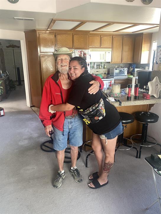 A joyful moment captured as a young woman hugs an elderly man in a friendly kitchen.