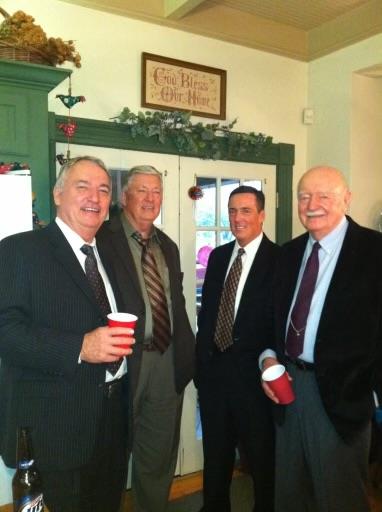 Friends dressed in suits hold red cups while socializing at a warm indoor celebration.