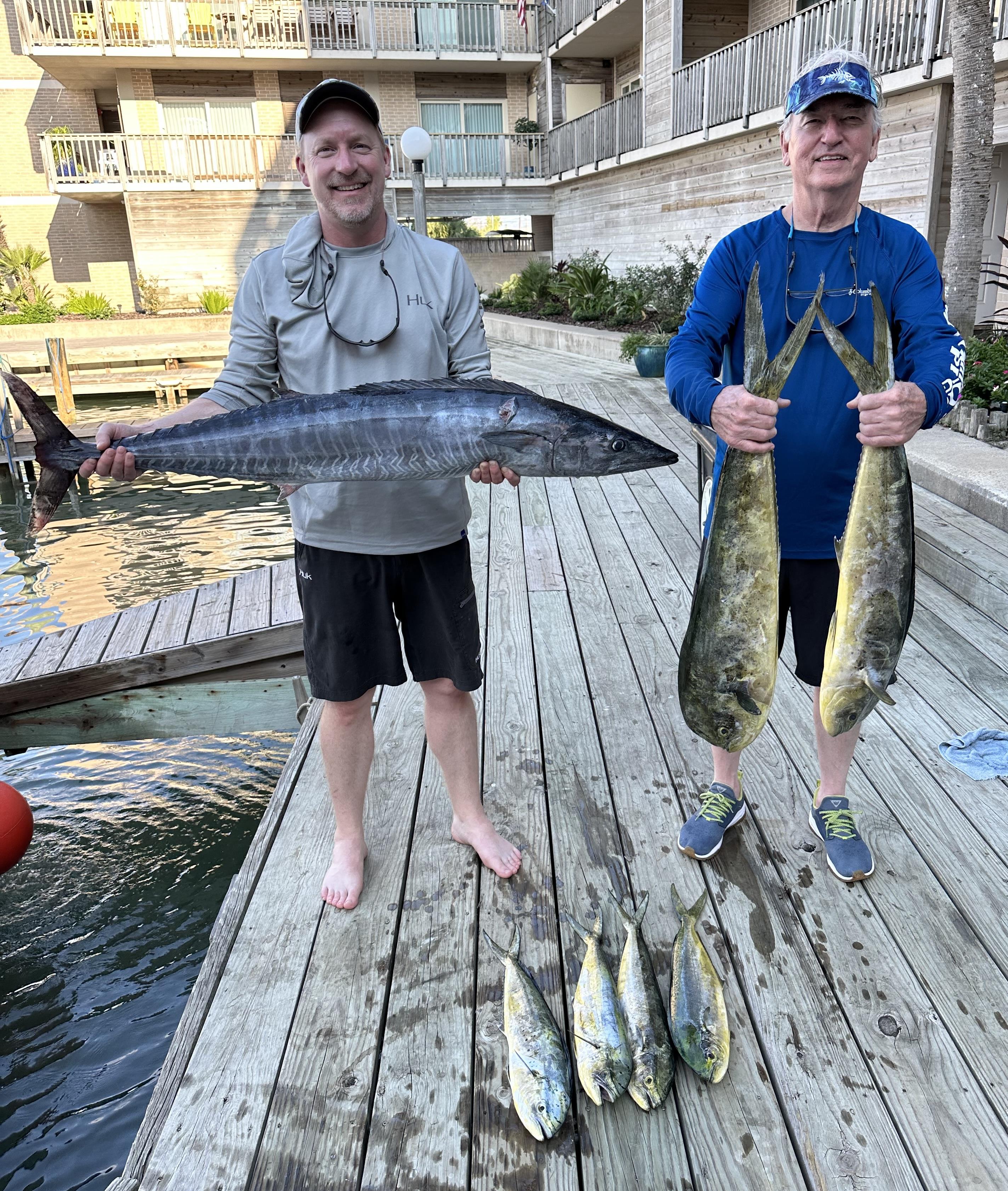 Two fishermen hold their impressive catch while standing on a wooden dock near the water.