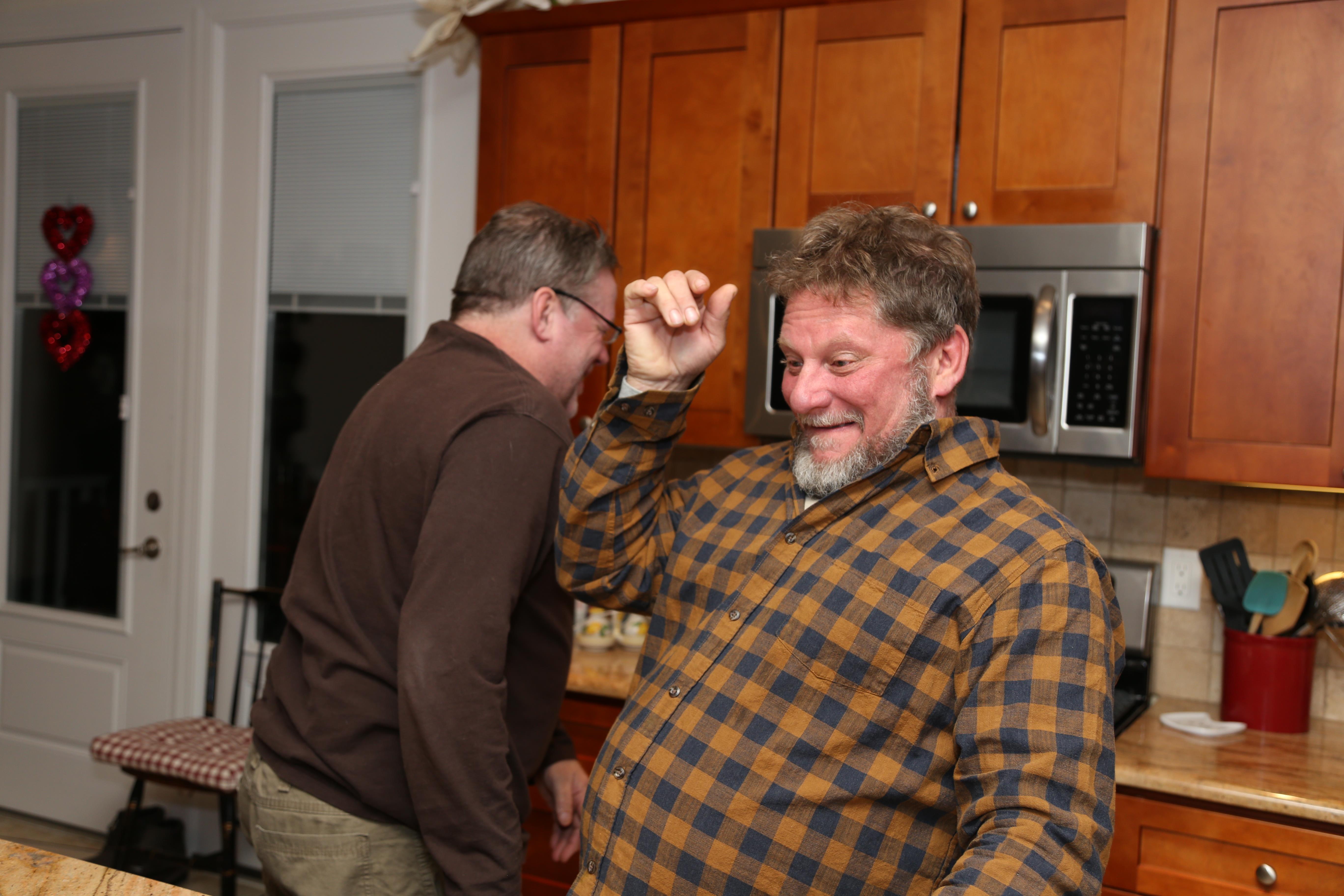 Two friends share a joyful moment while dancing in a warm kitchen during a gathering.
