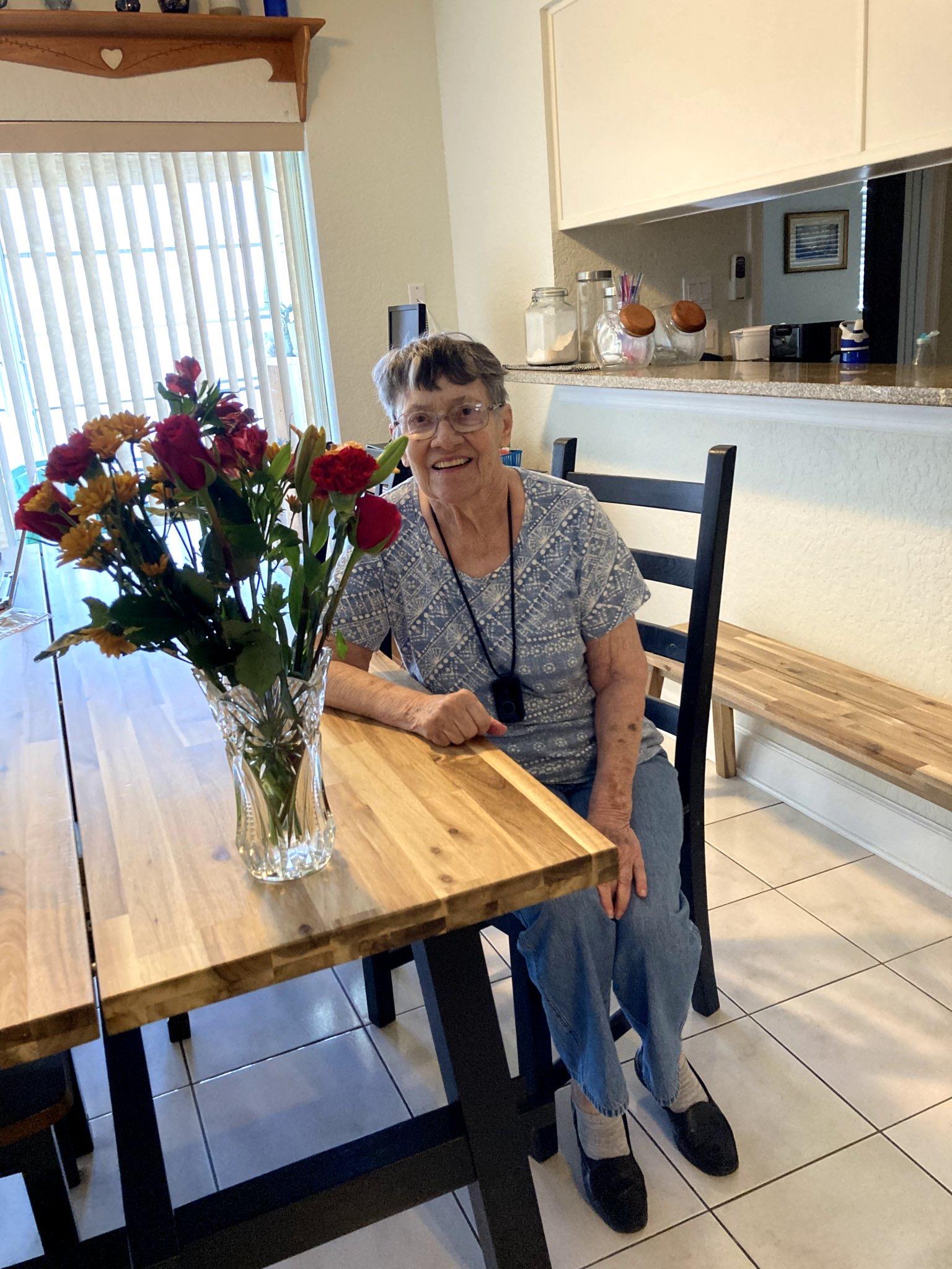 A woman enjoys the view of a vibrant flower bouquet while seated at her kitchen table.