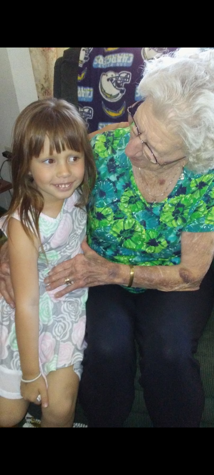 A young girl and her grandmother are sitting together, smiling and enjoying each other's company.