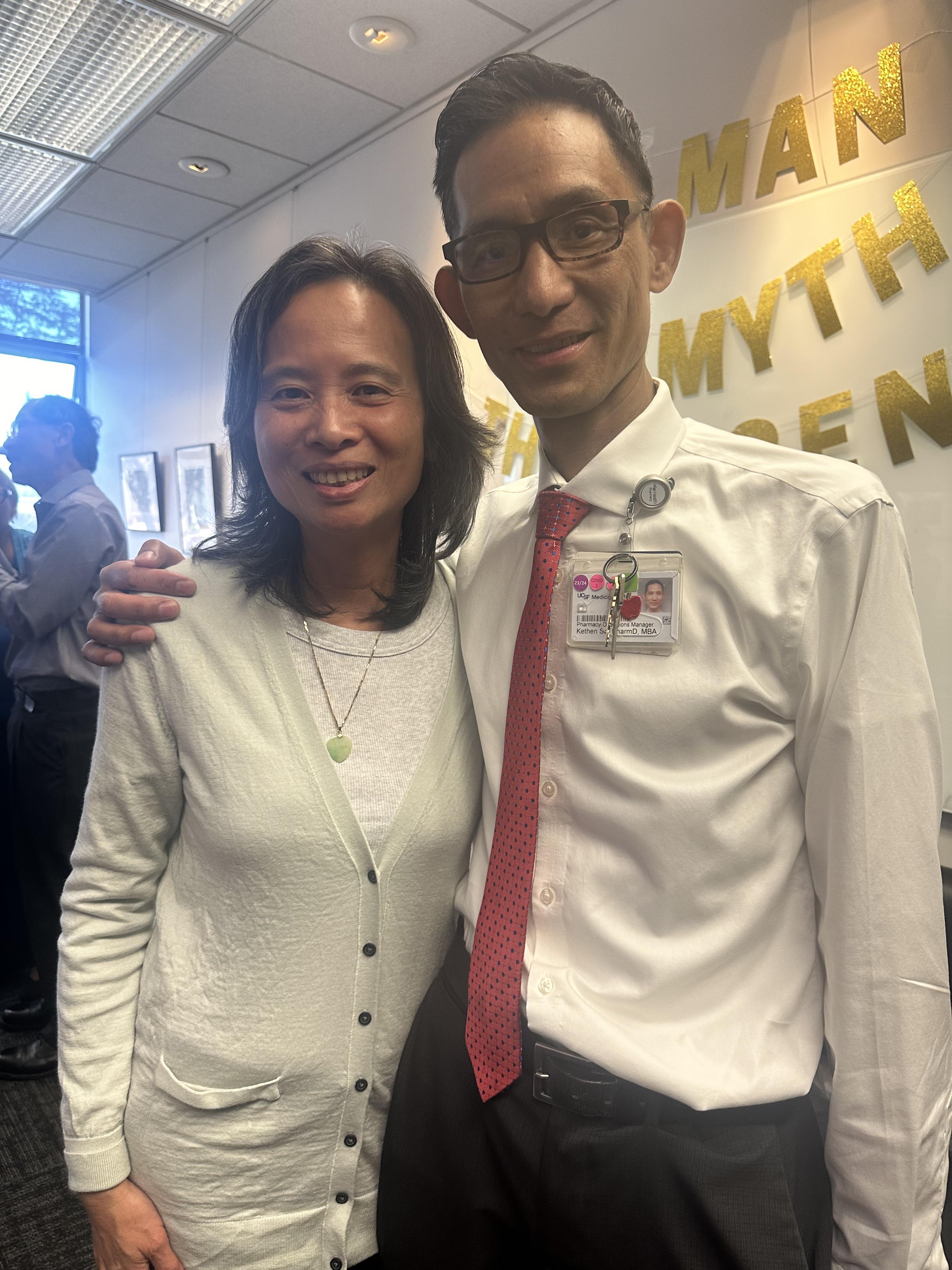 Two colleagues pose together during a celebratory event in an office setting.