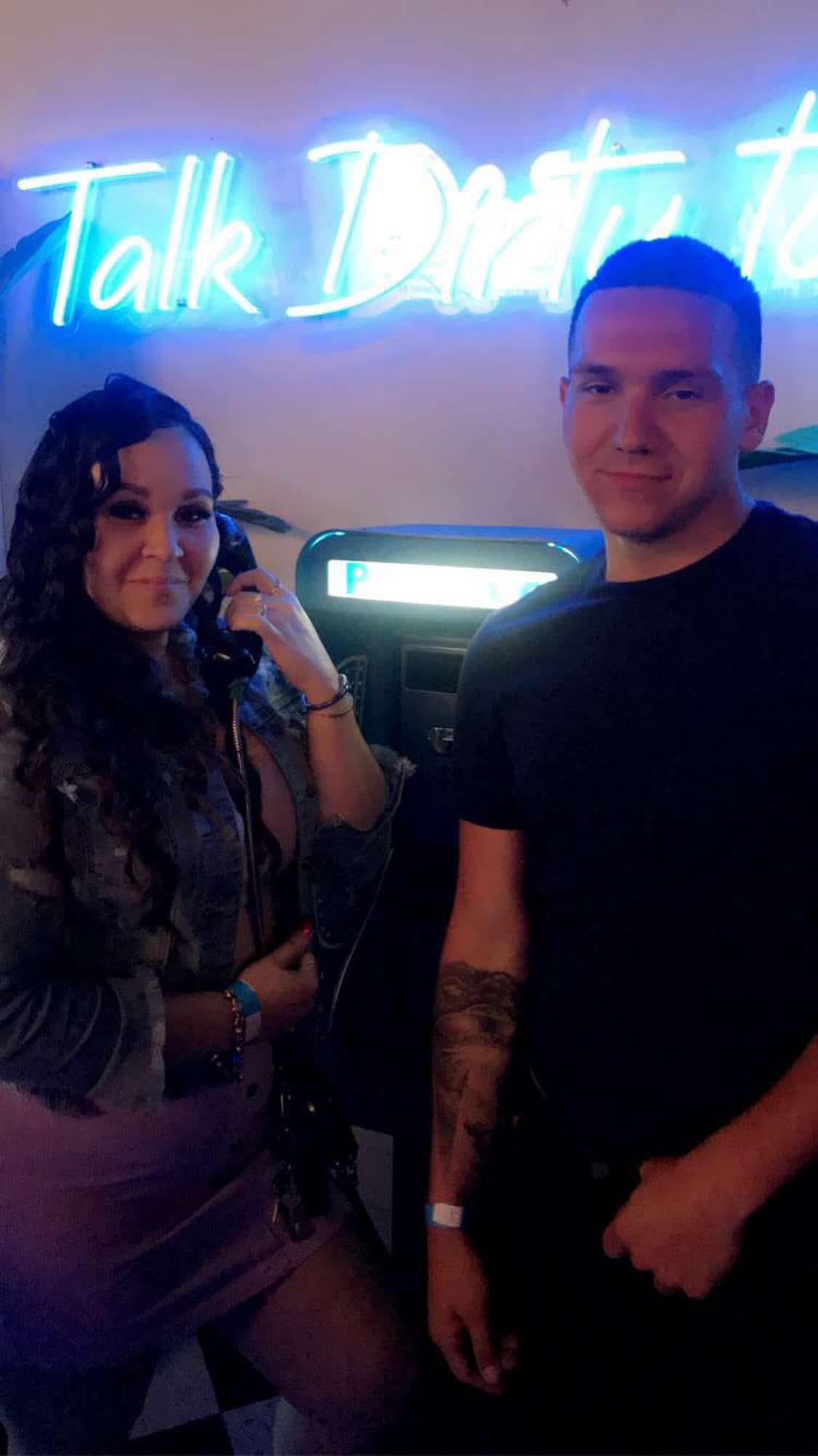 Two friends pose by a retro phone booth with a neon sign, enjoying a fun night out together.