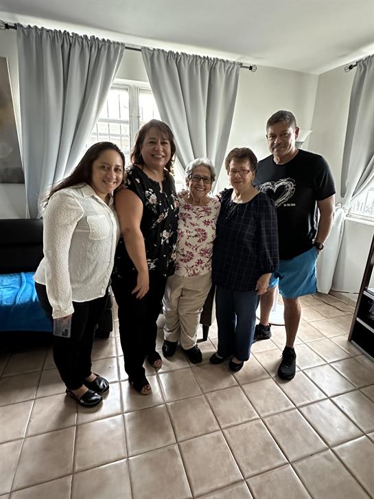 Five family members enjoy time together in a cozy living room setting, smiling warmly.