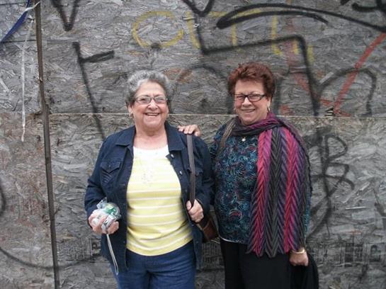 Two women stand side by side, sharing a joyful moment while enjoying the urban atmosphere.