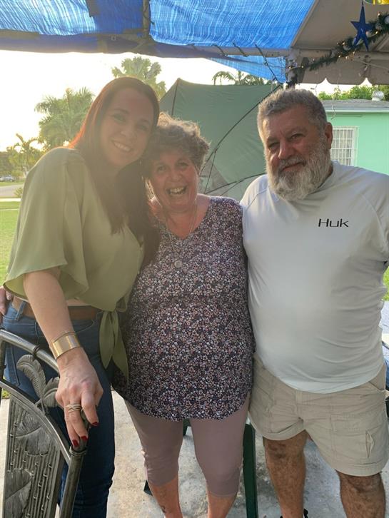 Three friends pose joyfully together on a sunny evening in a backyard setting.