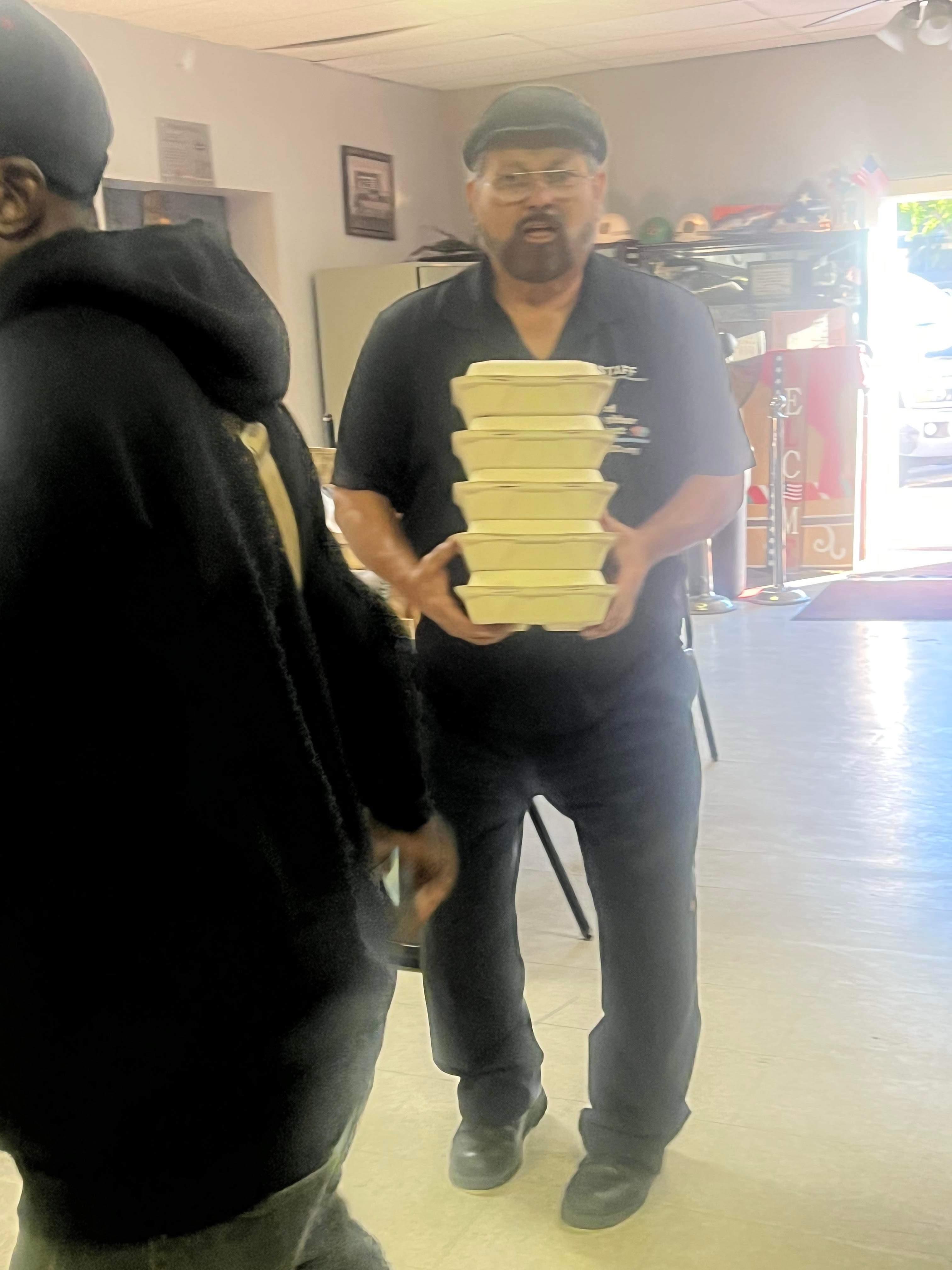 A person is balancing several food containers in a local community center during a busy activity.