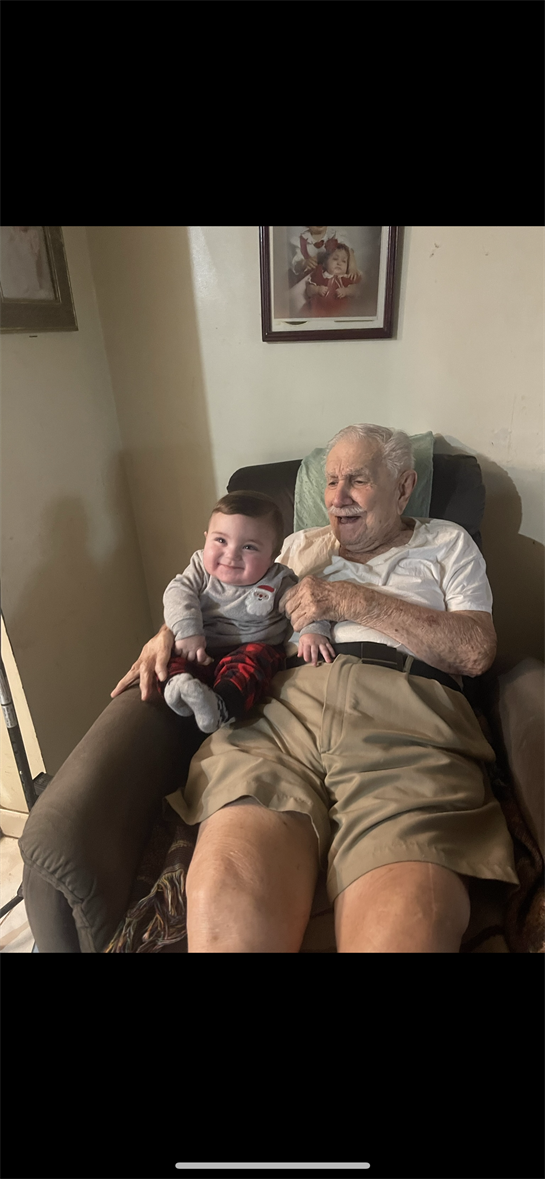 A grandfather smiles warmly while holding his laughing grandchild on a comfy chair.