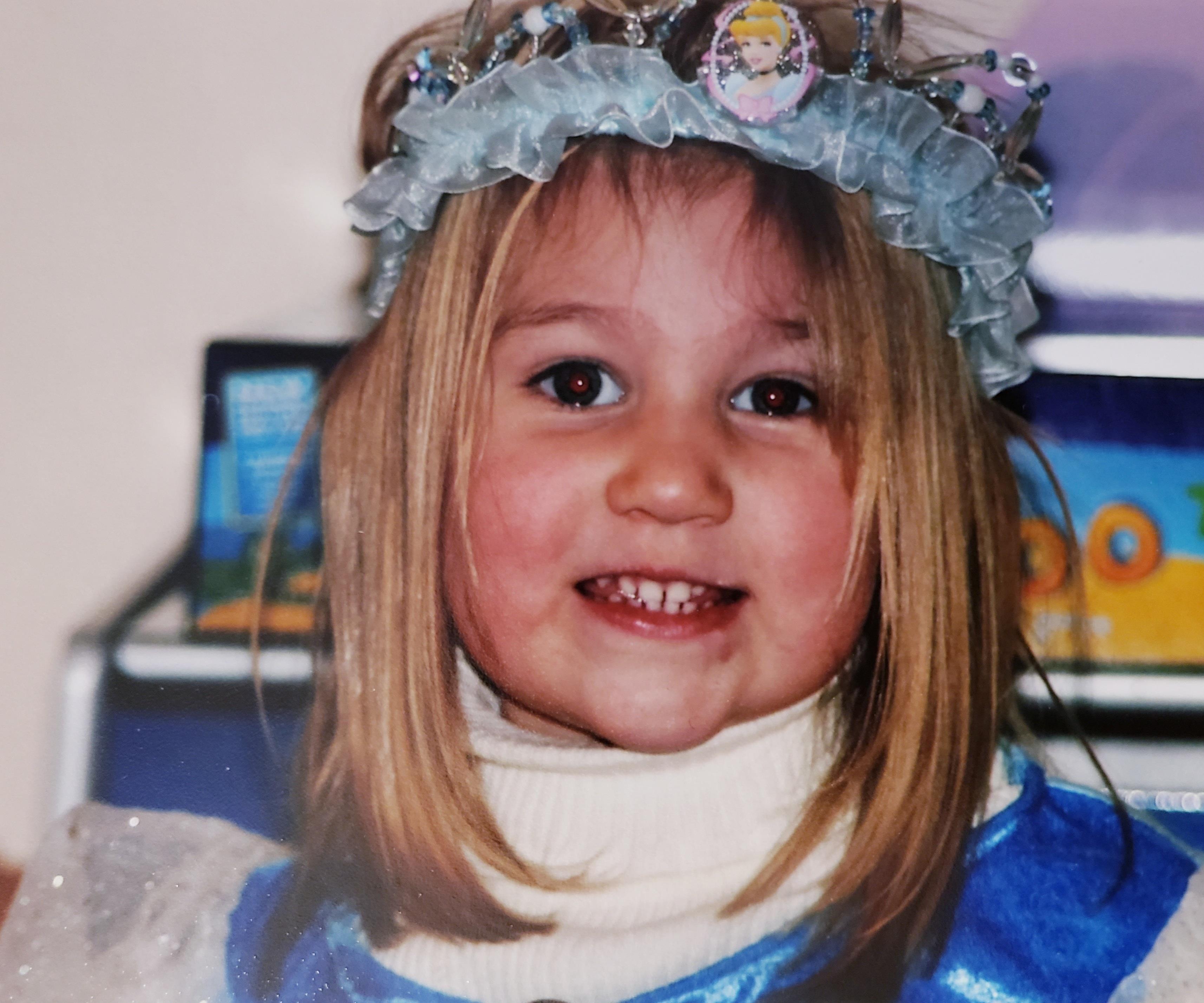 A young girl smiles brightly while wearing a princess costume and floral crown at a festive event.