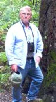 A person is dressed casually in jeans and a light shirt, standing in a forest.