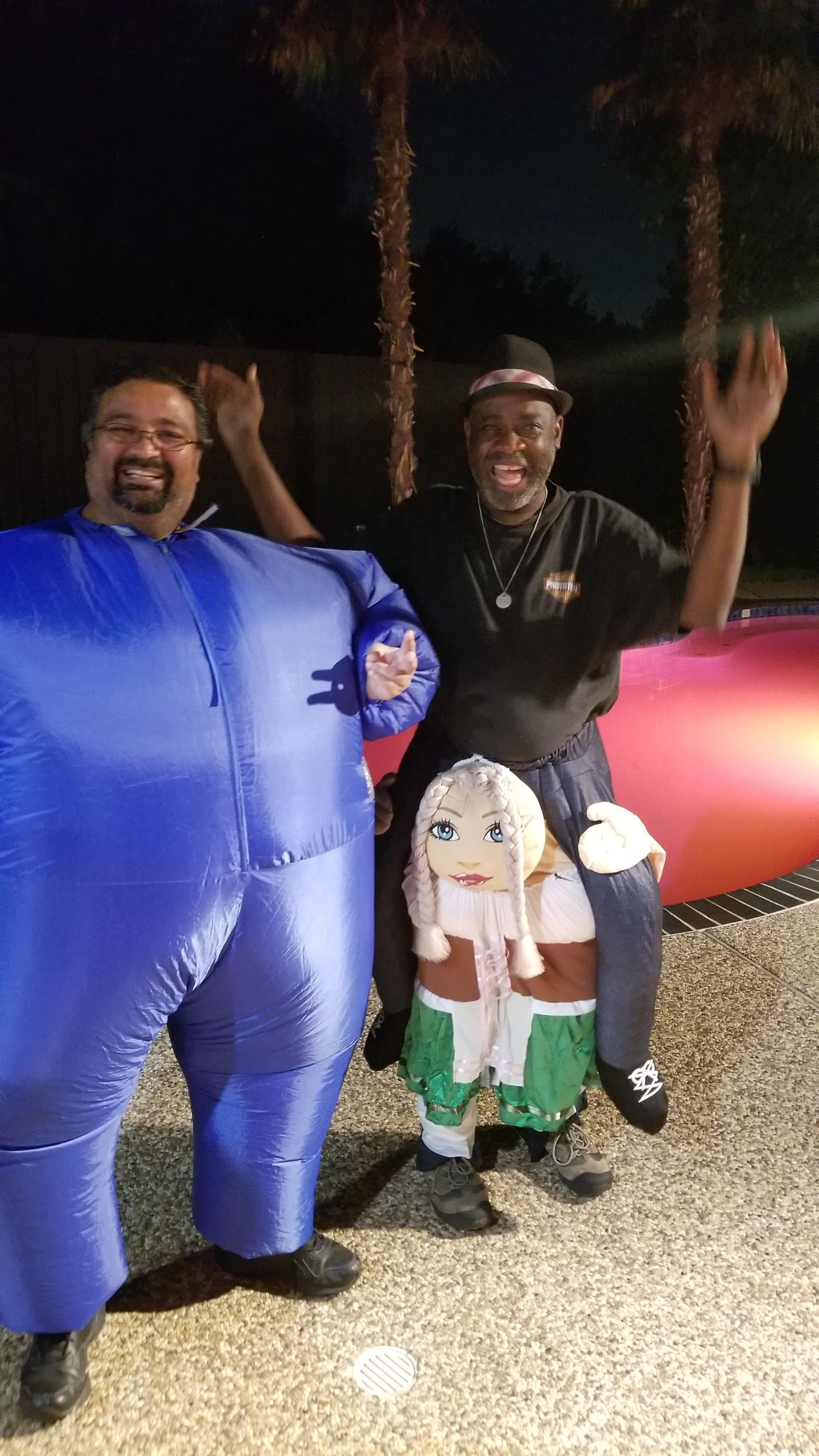 Two friends wearing inflatable costumes celebrate joyfully at a nighttime gathering.