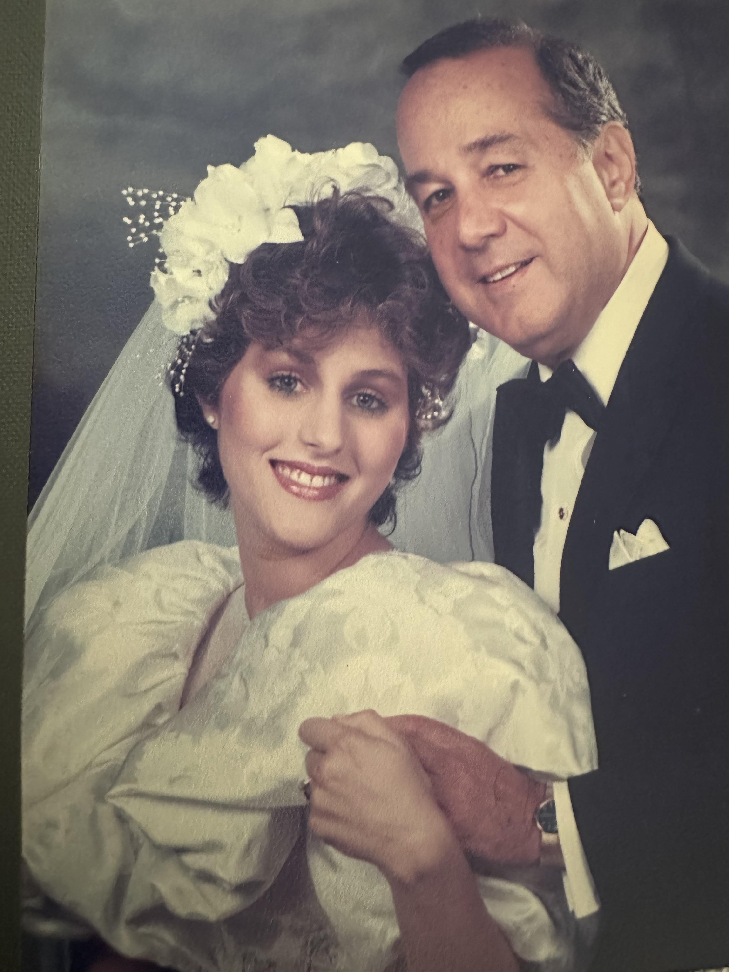 Bride and groom embrace joyfully while posing in formal wedding attire with a soft background.