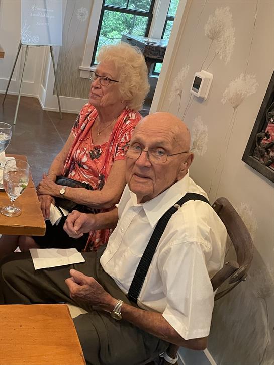 An elderly couple sits together at a table, sharing a meal and conversation in a cozy setting.