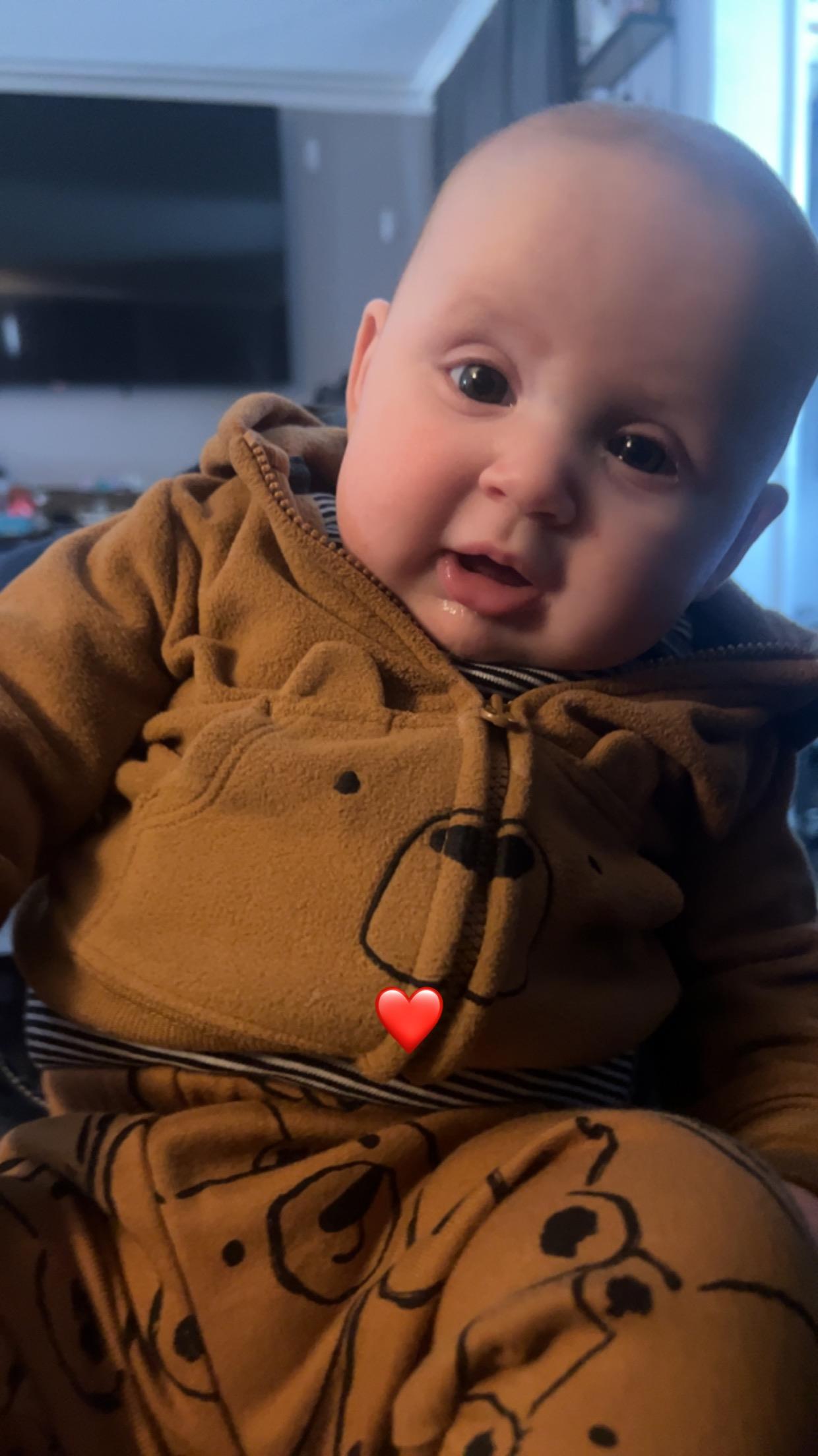 A joyful baby is seated comfortably in a cozy bear outfit, smiling in warm lighting at home.
