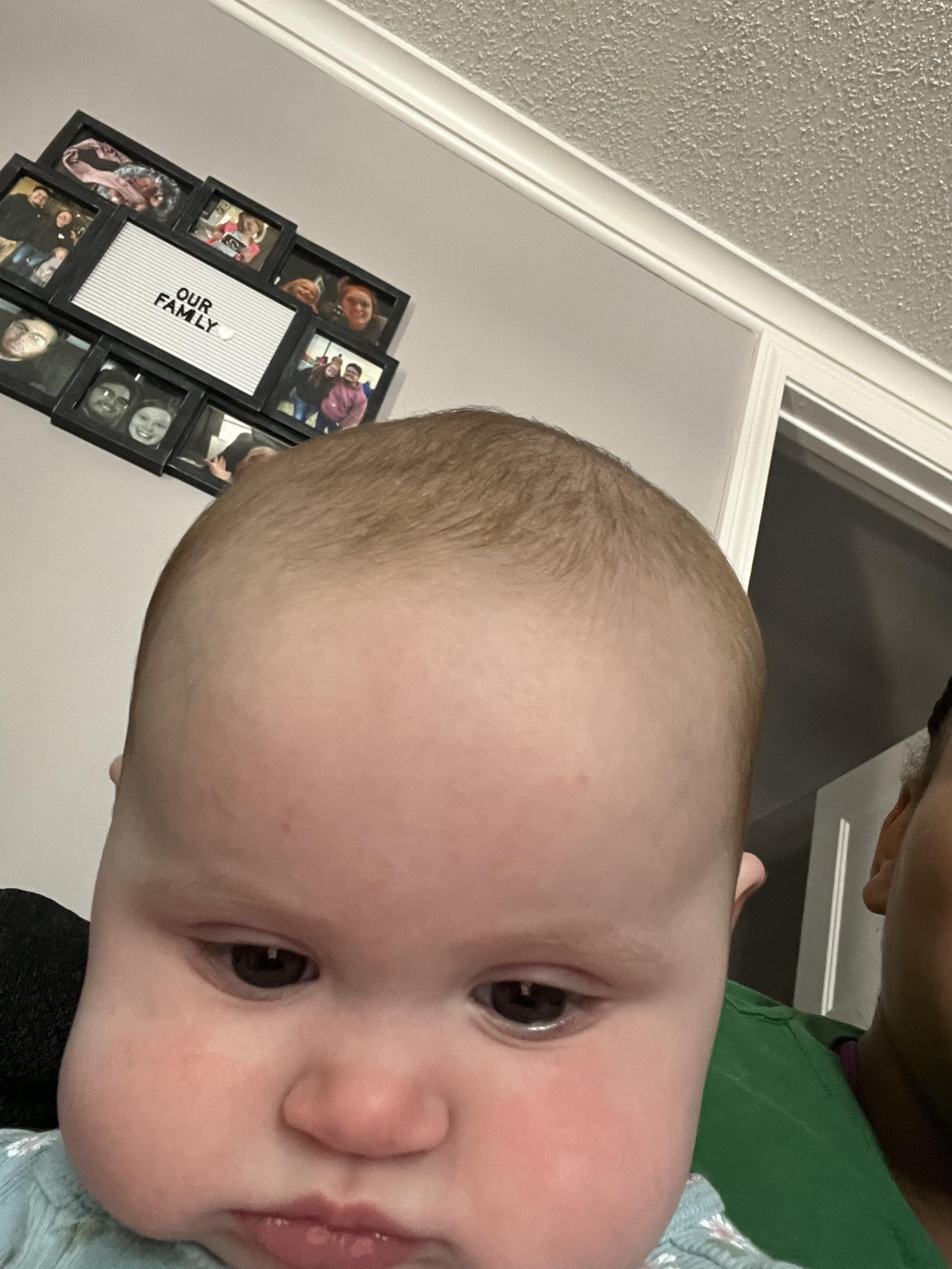 A baby shows curiosity while exploring the living room with family photos nearby.