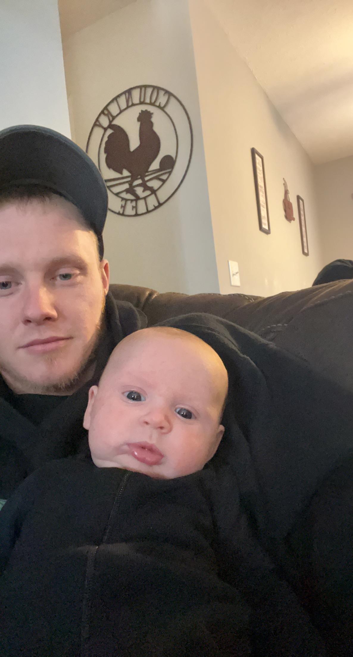 A father holds his baby close, both looking relaxed and content in their living room.