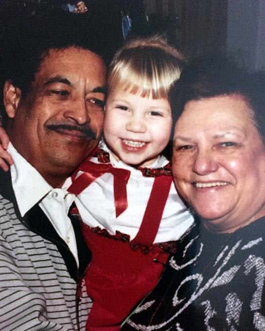 Grandparents joyfully embrace their smiling granddaughter in cozy winter clothing.