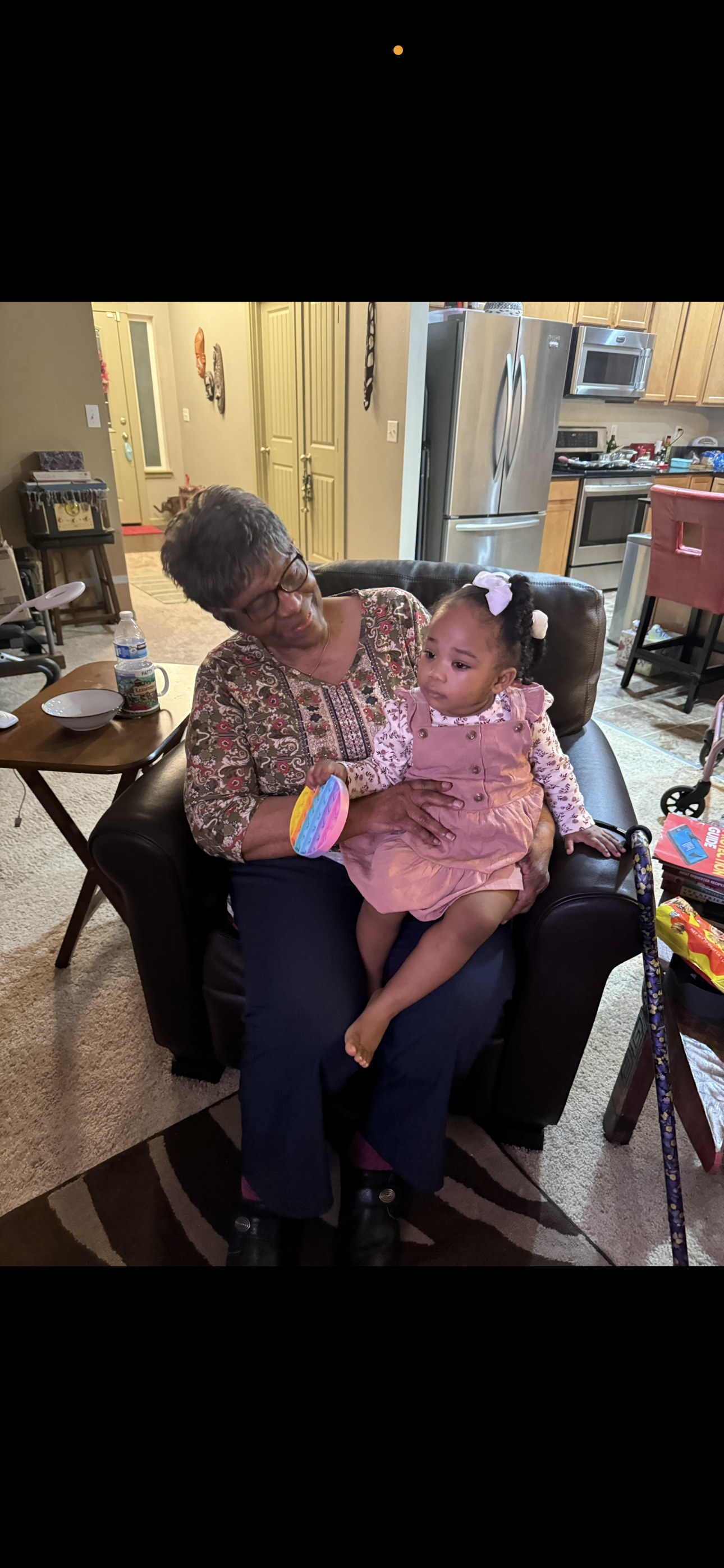 A grandmother and her granddaughter share a moment in a comfortable living room surrounded by toys.