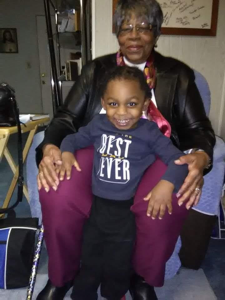A grandmother sits comfortably with her smiling grandson on her lap, enjoying family time.