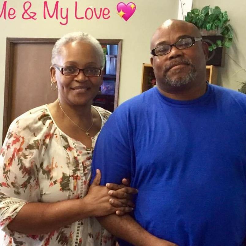 A couple smiles together in a cozy indoor space filled with plants.