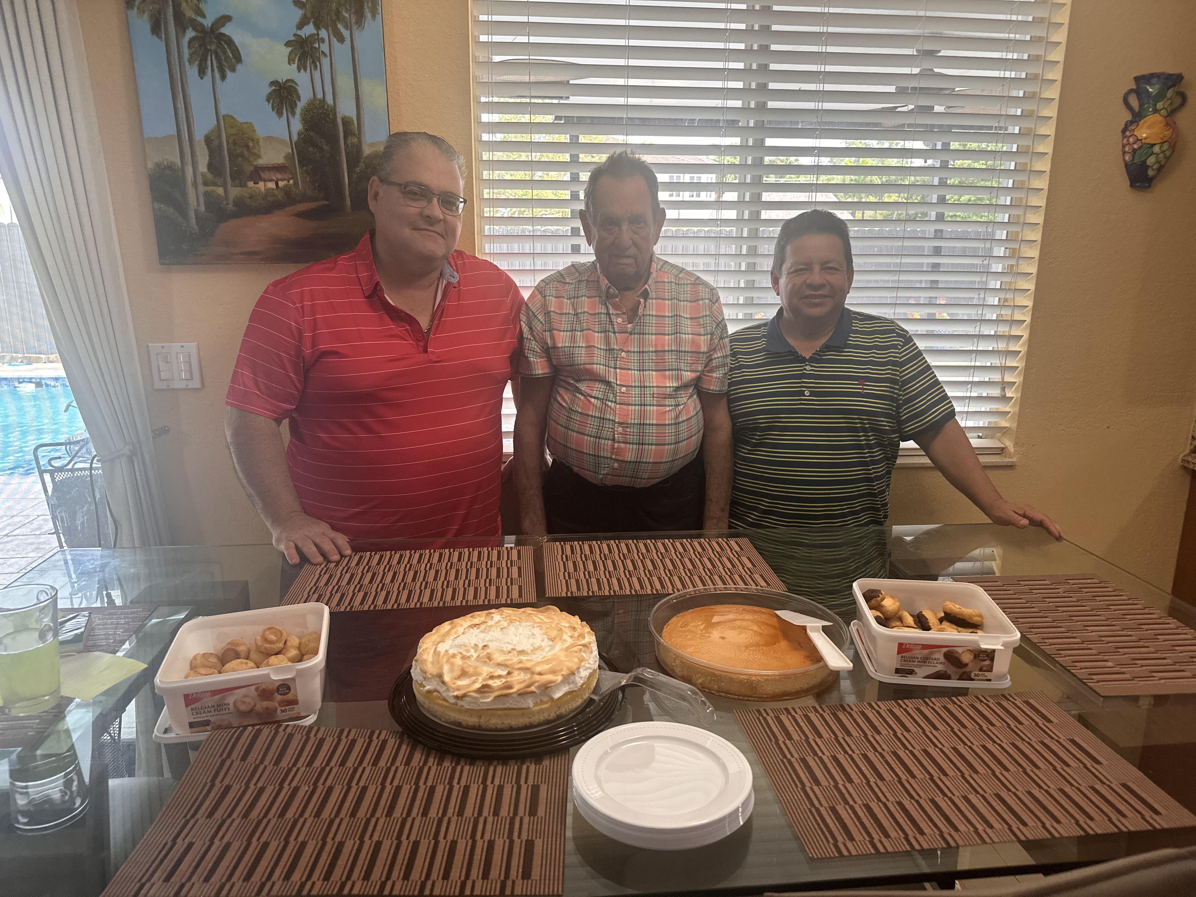 Three friends smile behind a table of desserts, celebrating their friendship.