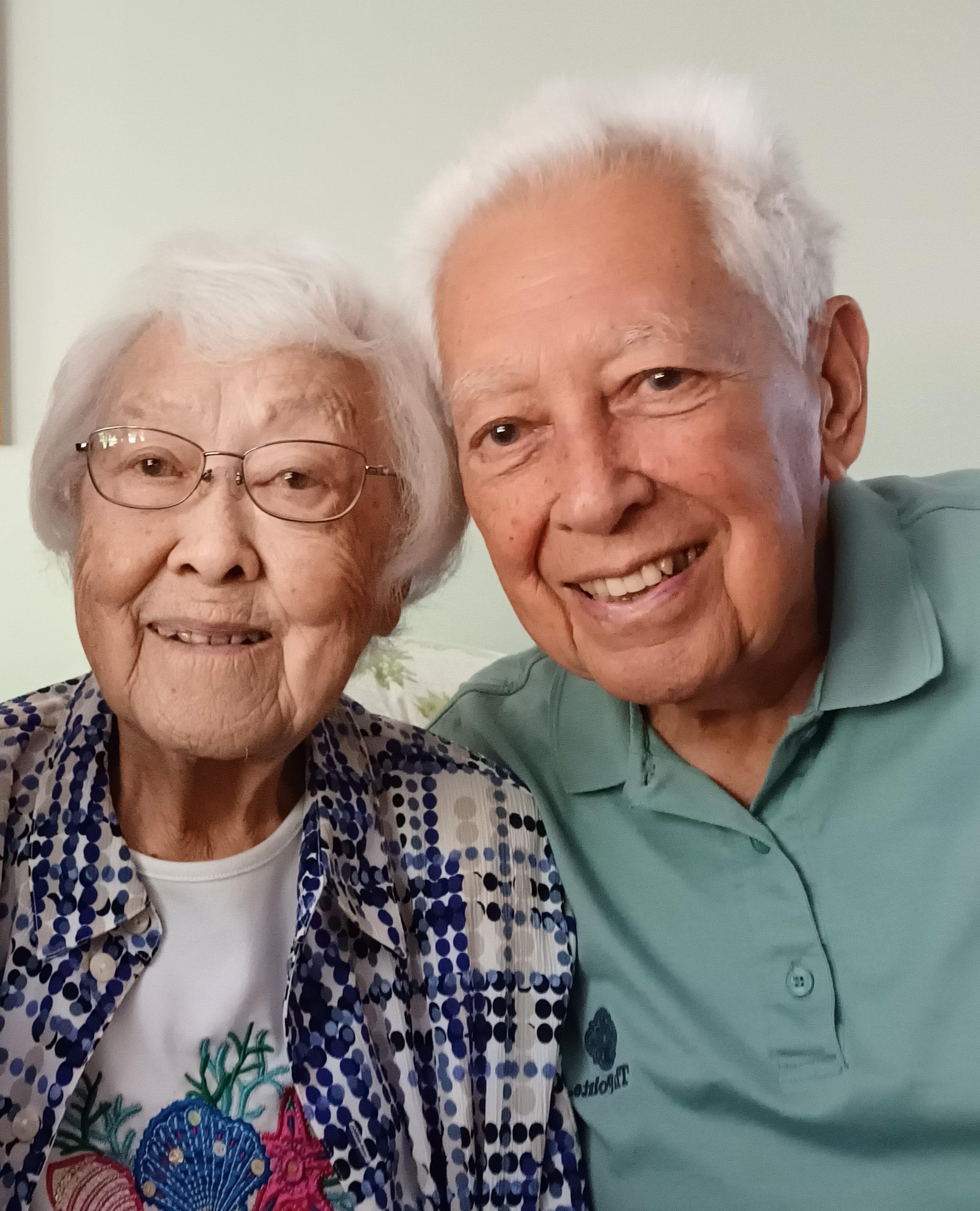 An elderly couple enjoys a joyful moment together, smiling warmly while sitting at home.