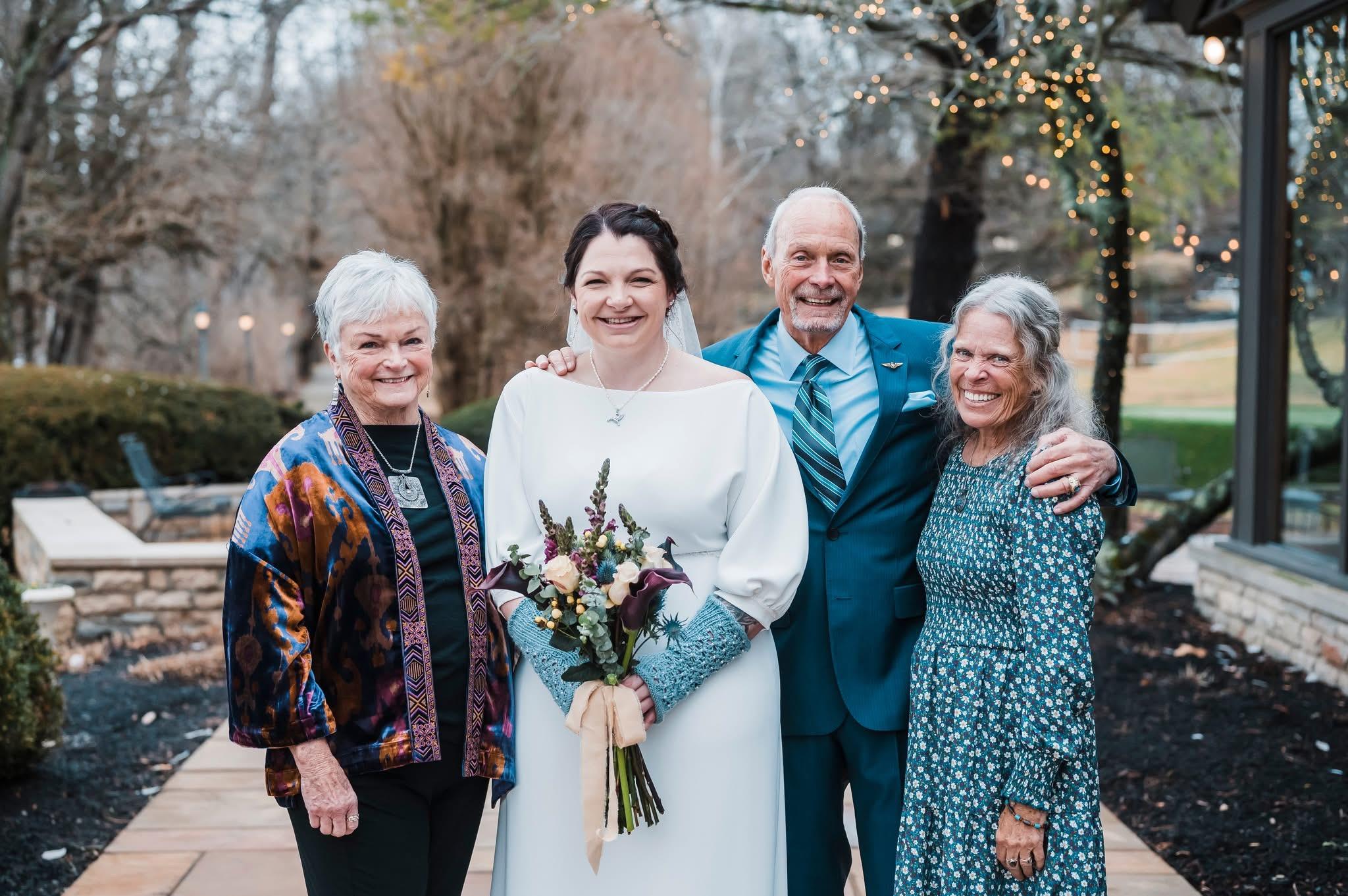 Four family members appear joyful together, celebrating a wedding outdoors in a scenic setting.