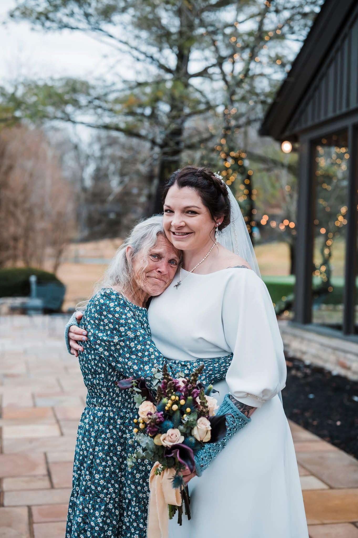 A bride holds her grandmother close, sharing a heartfelt moment outdoors during the wedding.
