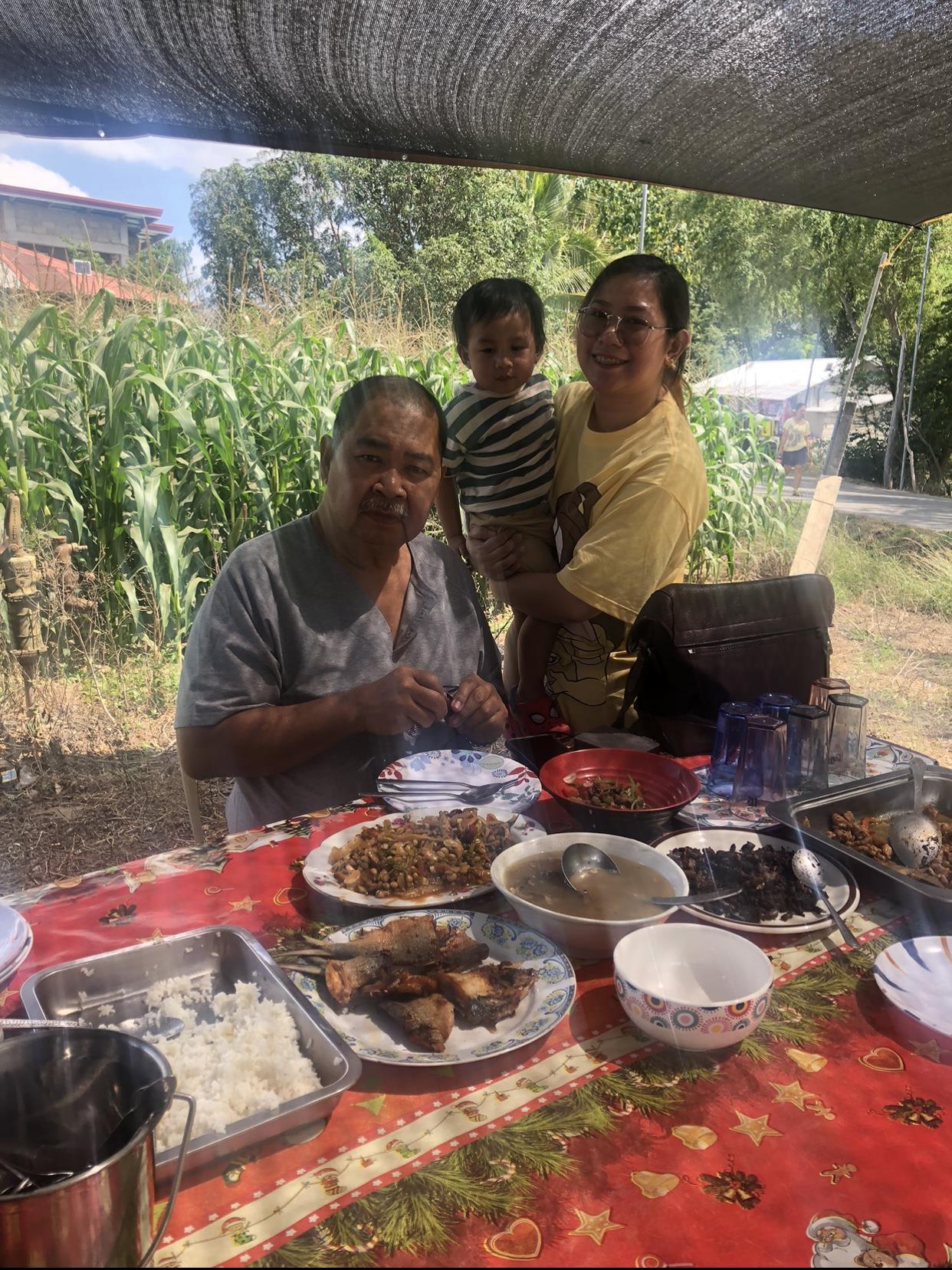 A family sits at a table filled with delicious food in a serene outdoor location.