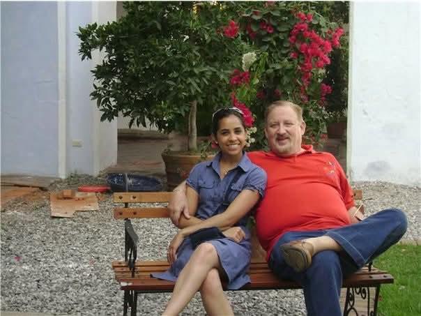 Two people enjoy each other's company on a bench in a vibrant garden filled with flowers.