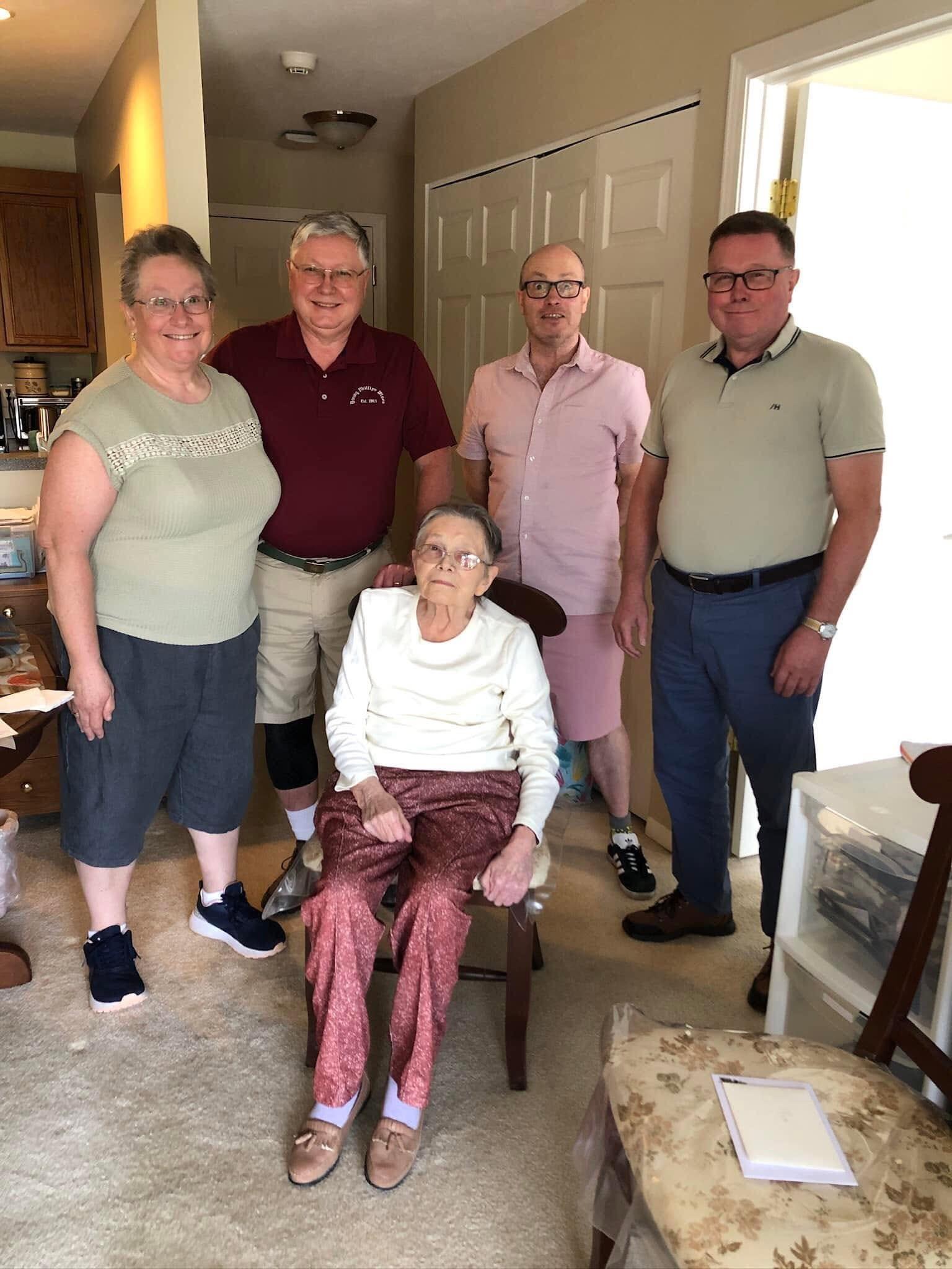 Relatives smiling together in a comfortable living room with an elderly woman sitting.