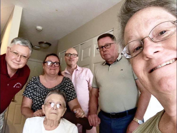 Family members gathered around, smiling and enjoying each other's company in a living room setting.