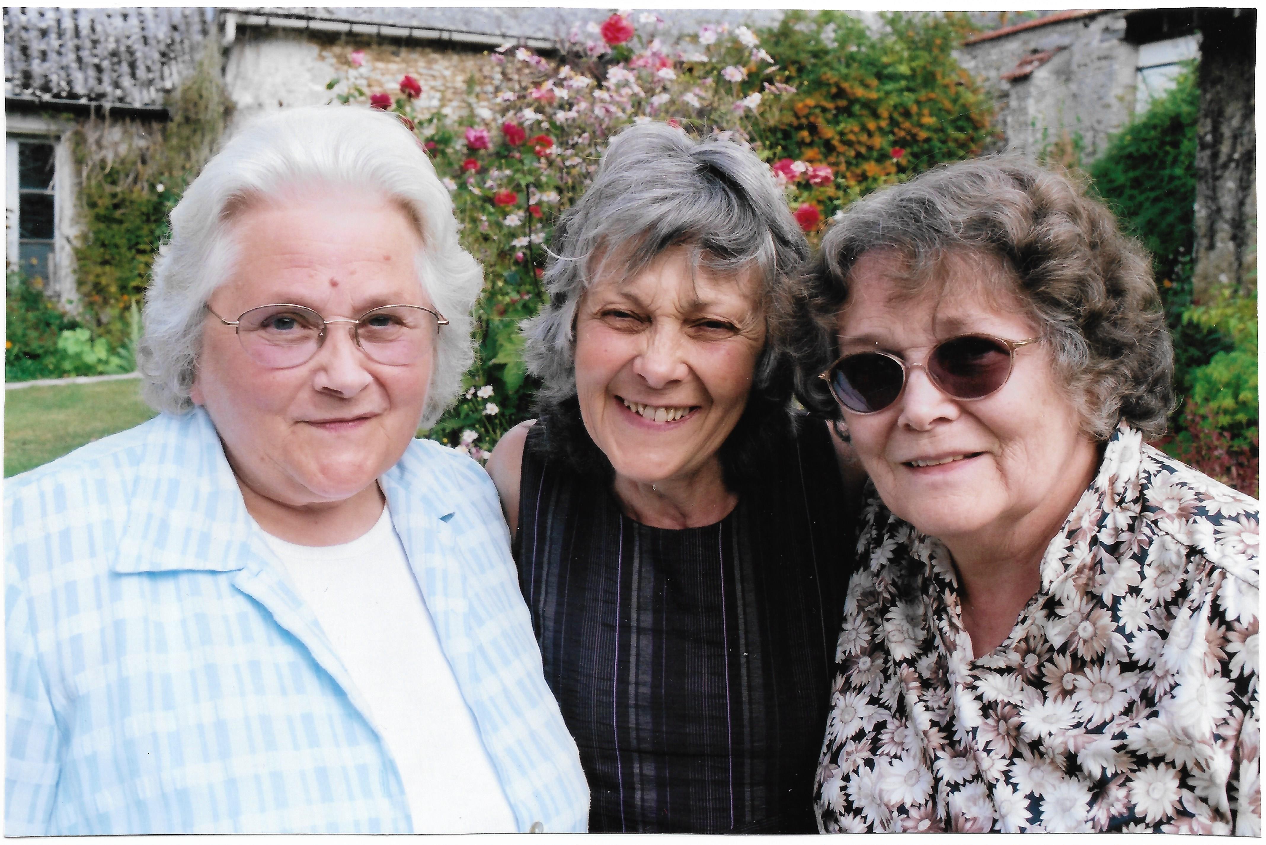Three women share happy smiles during a reunion celebration in a beautiful garden setting.