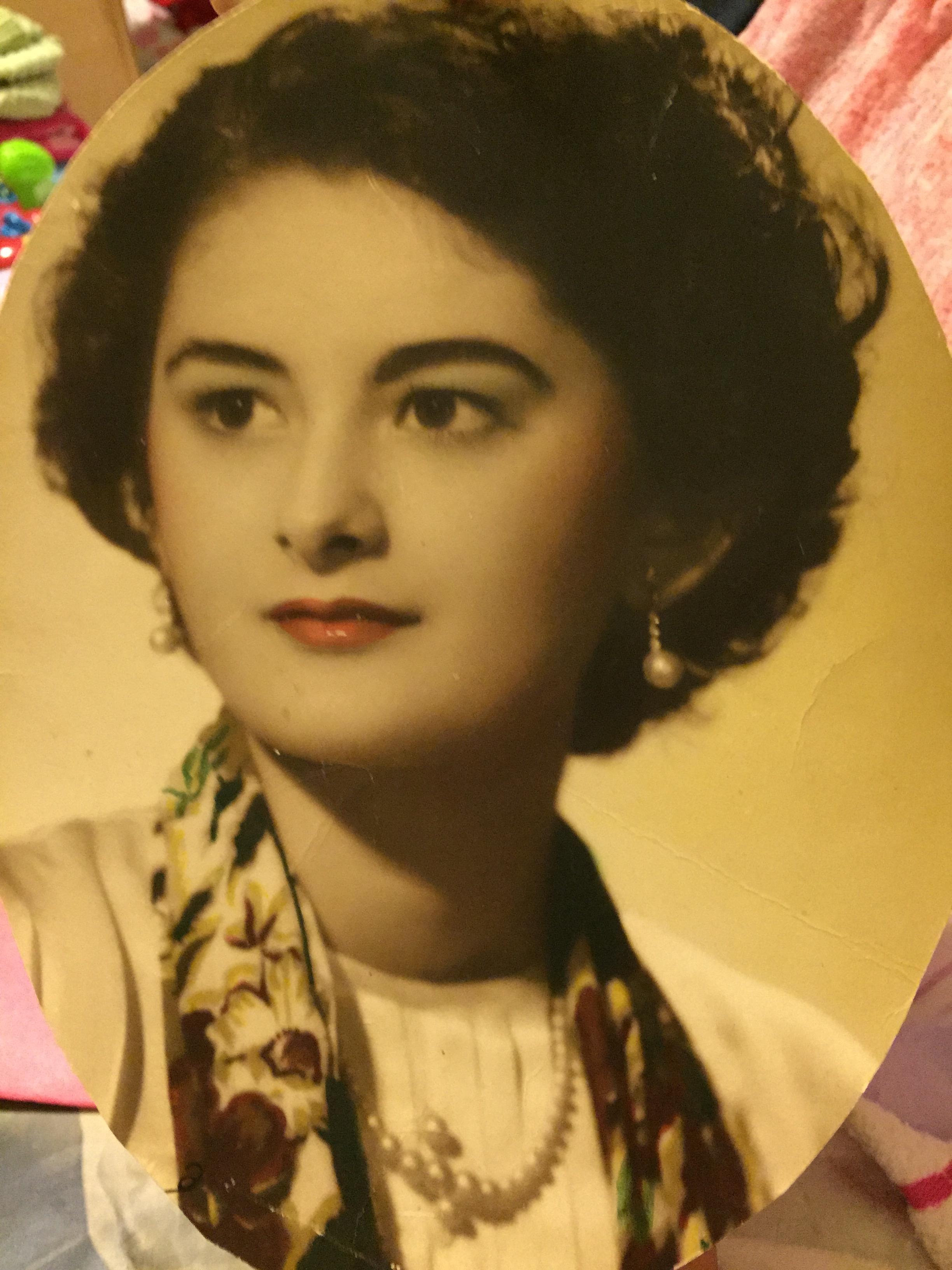 A woman poses gracefully, displaying a classic hairstyle and pearl accessories from a past era.