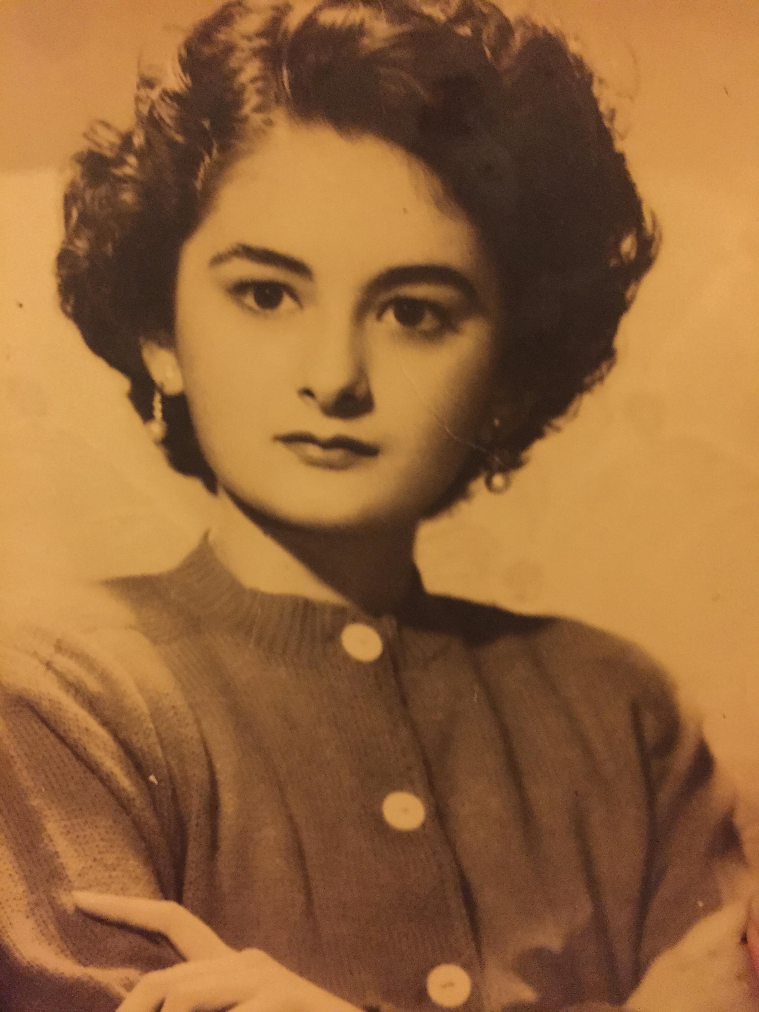 A young woman poses confidently with crossed arms, showcasing mid-20th century fashion.