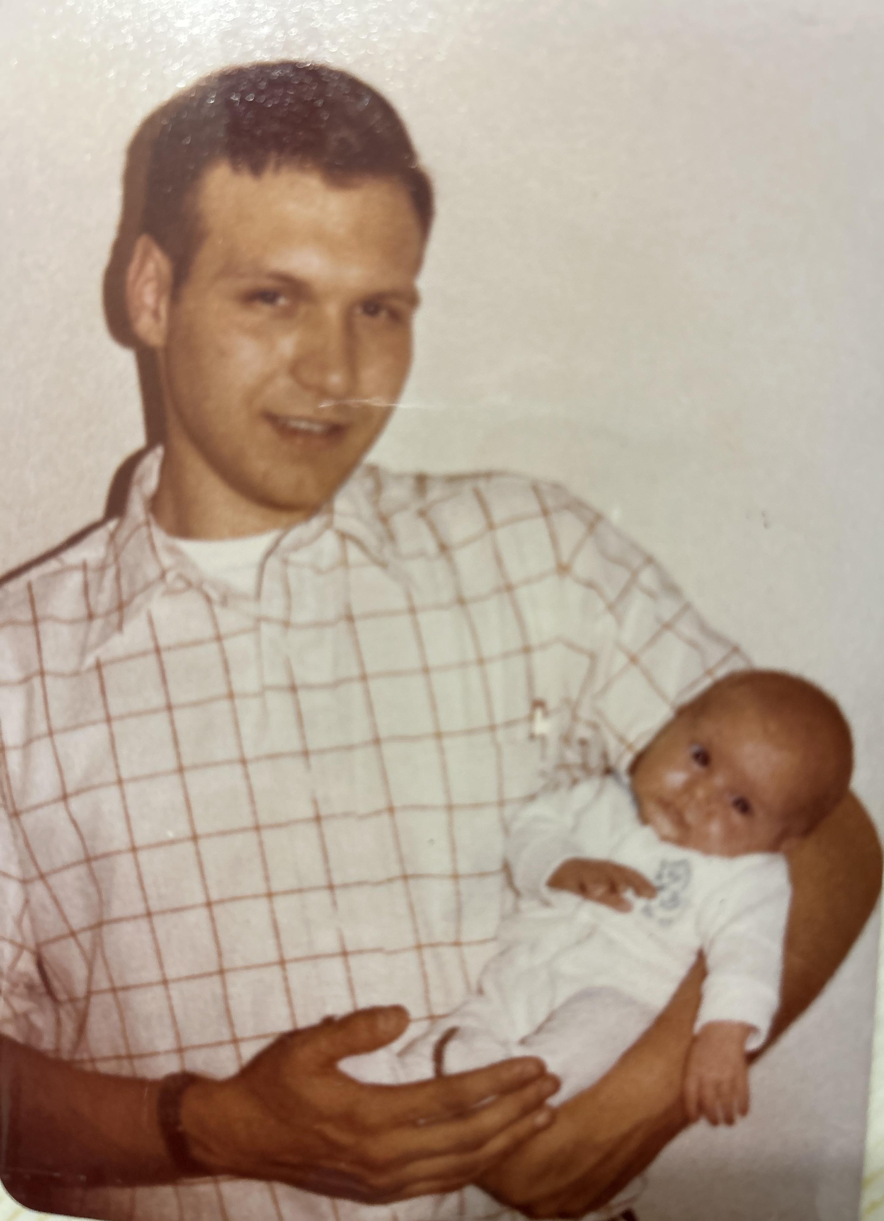 A proud father cradles his newborn baby in a warm, intimate indoor environment.