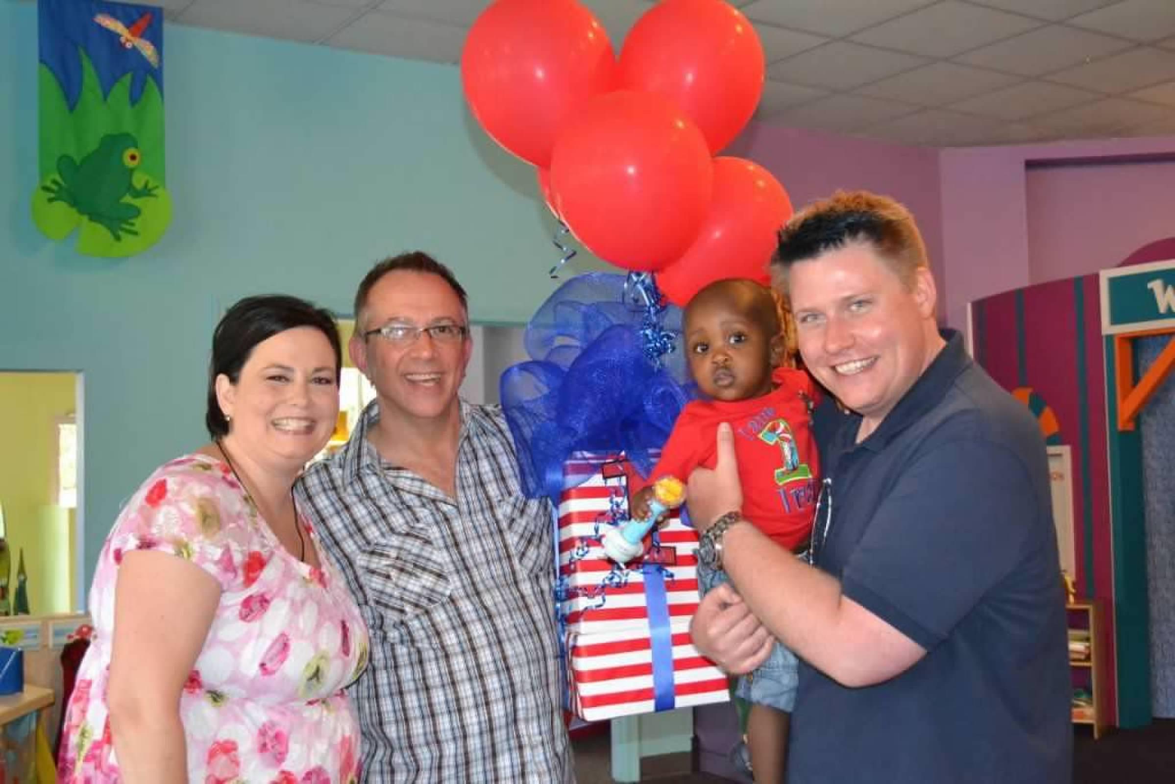 Family and friends gather to celebrate a child's birthday with balloons and gifts.
