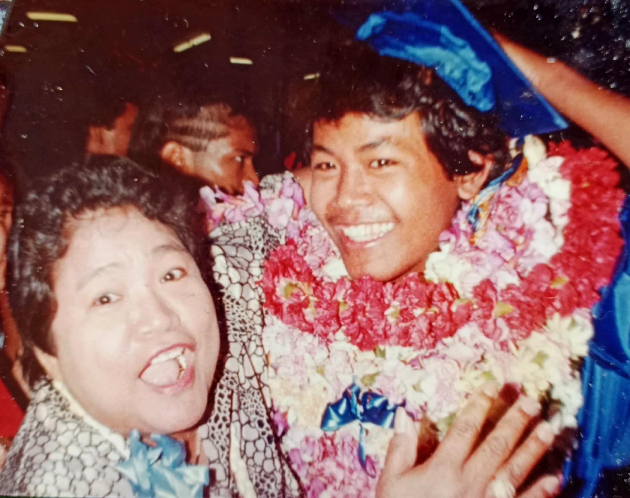 Two individuals joyfully celebrate adorned in vibrant floral leis at a festive gathering.