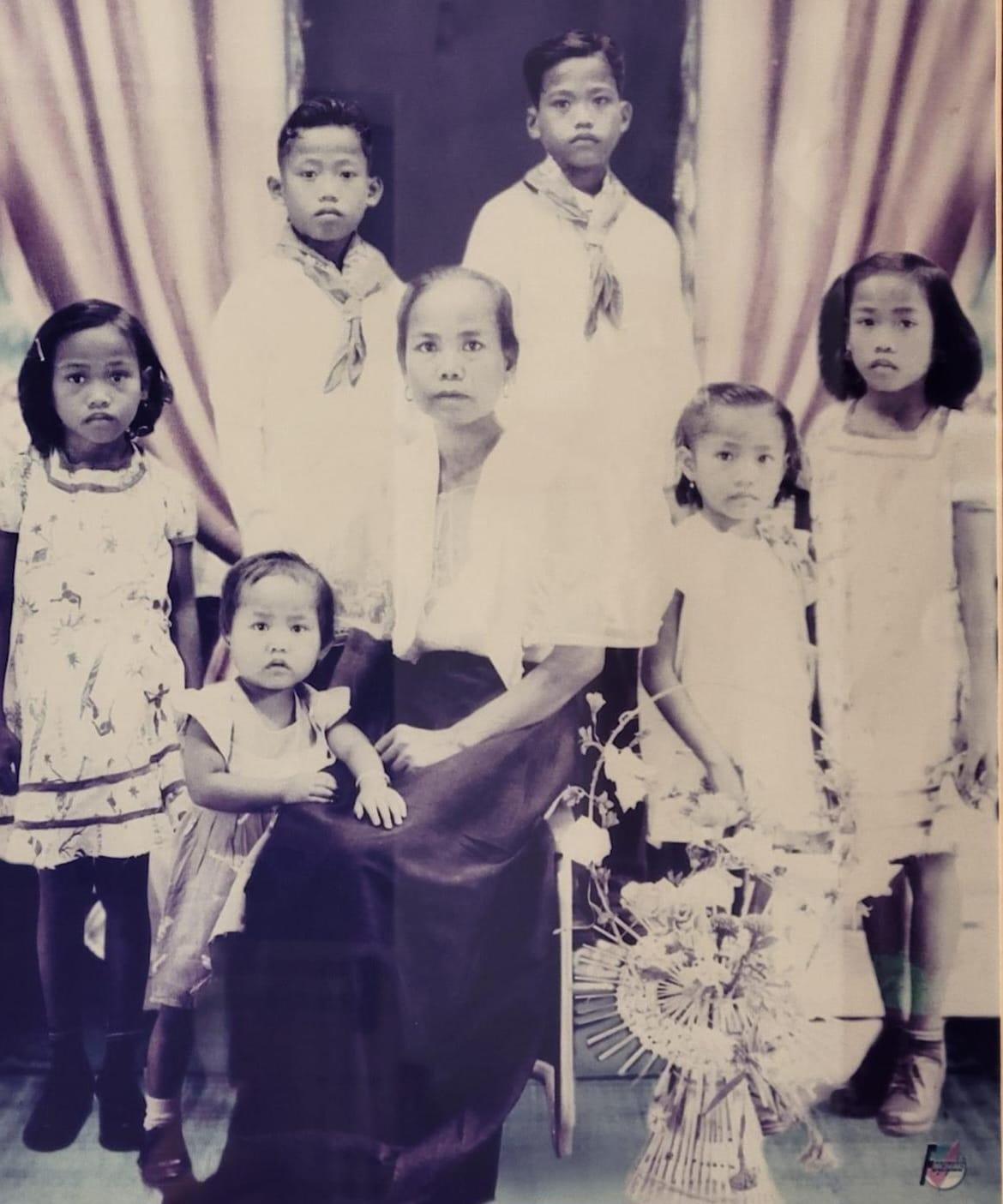 A group of children and an adult woman pose together, dressed formally, in an elegant interior.